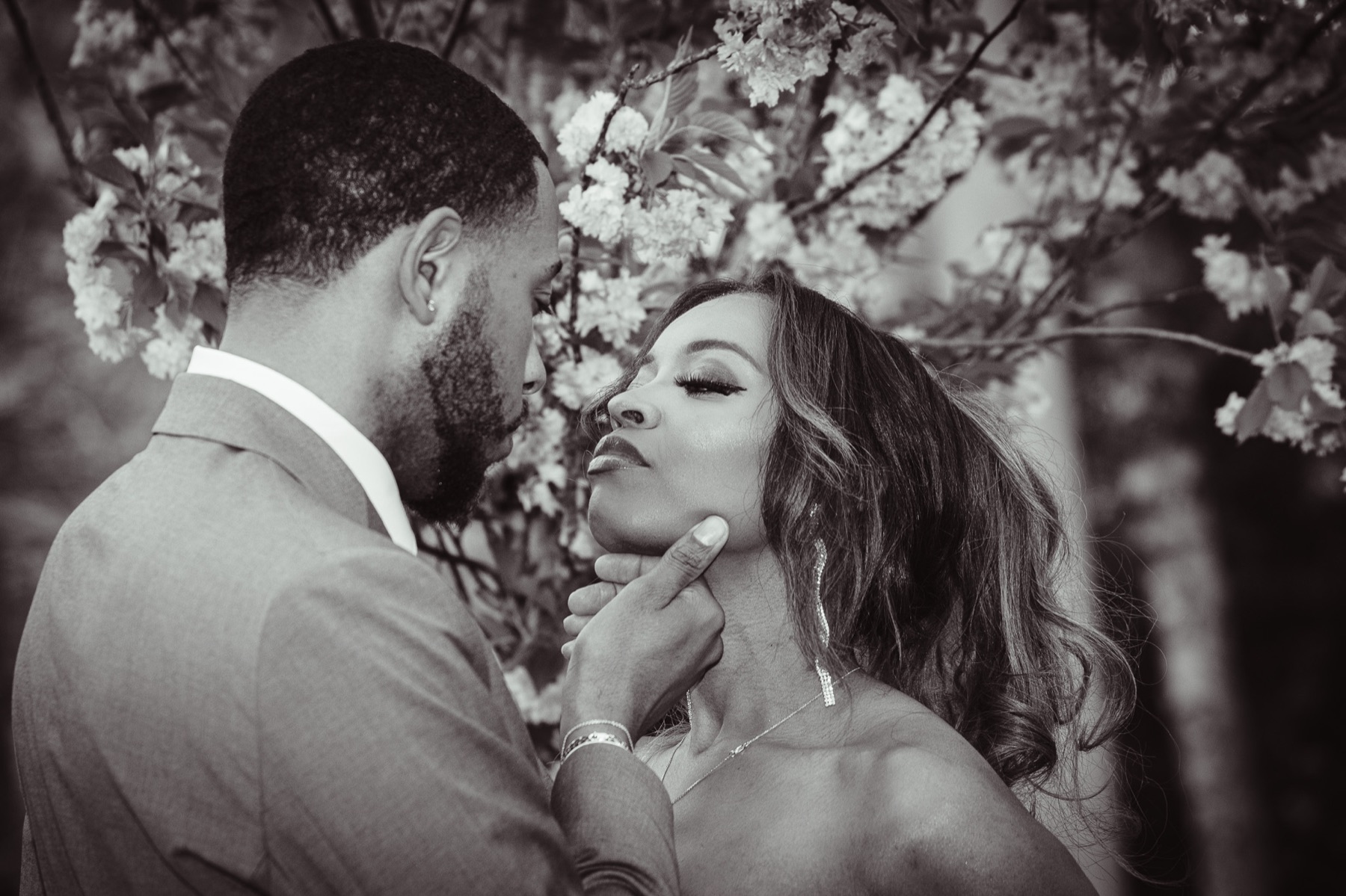 Jelani lifts Kimberly's chin beneath white blossoms, in black and white