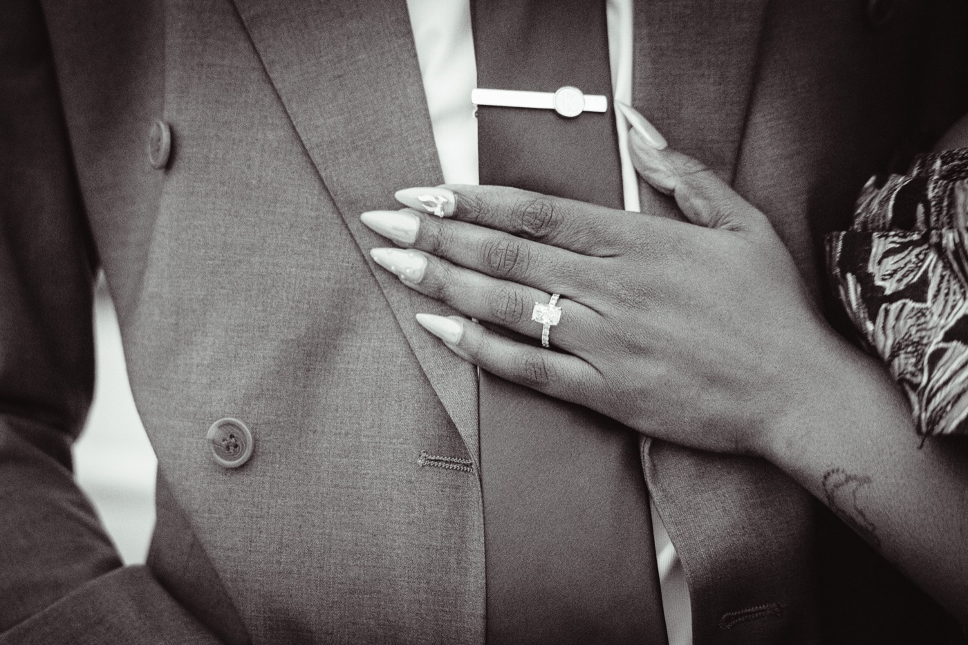 Kimberly's hand with her engagement ring resting on Jelani's lapel