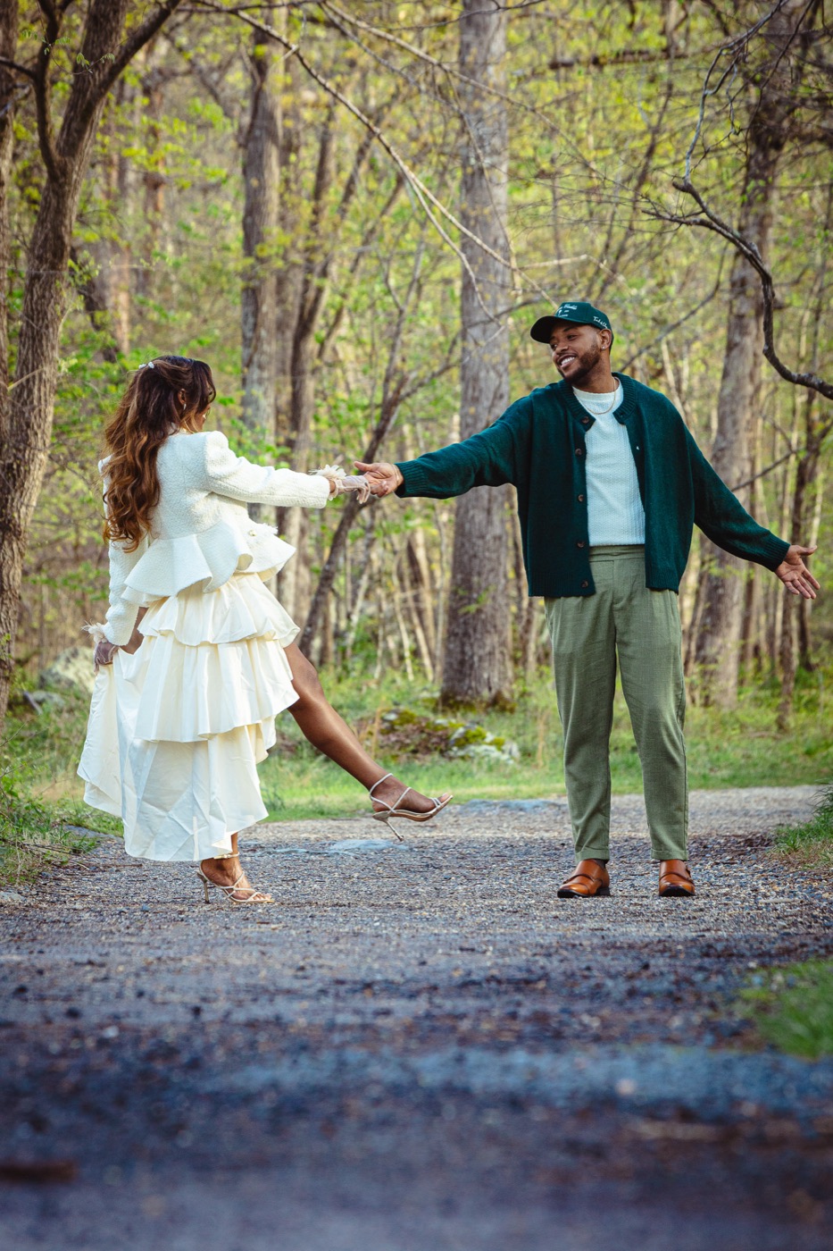 Kimberly kicking up her heel in an ivory ruffled skirt as Jelani reaches for her hand on a woodland path