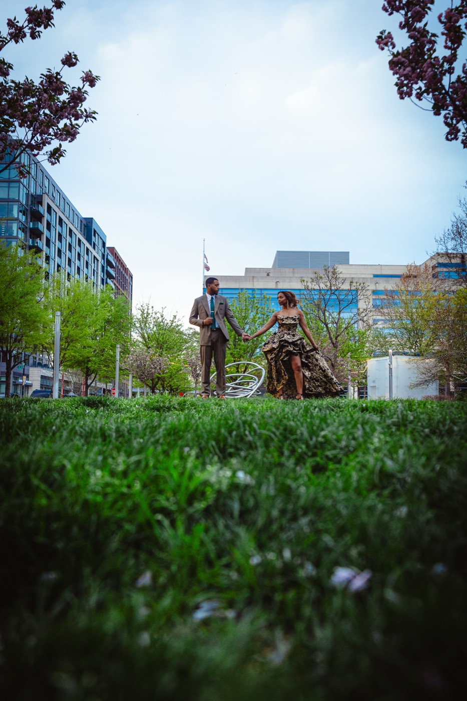 Kimberly in a gold brocade gown and Jelani in a suit holding hands on a city lawn